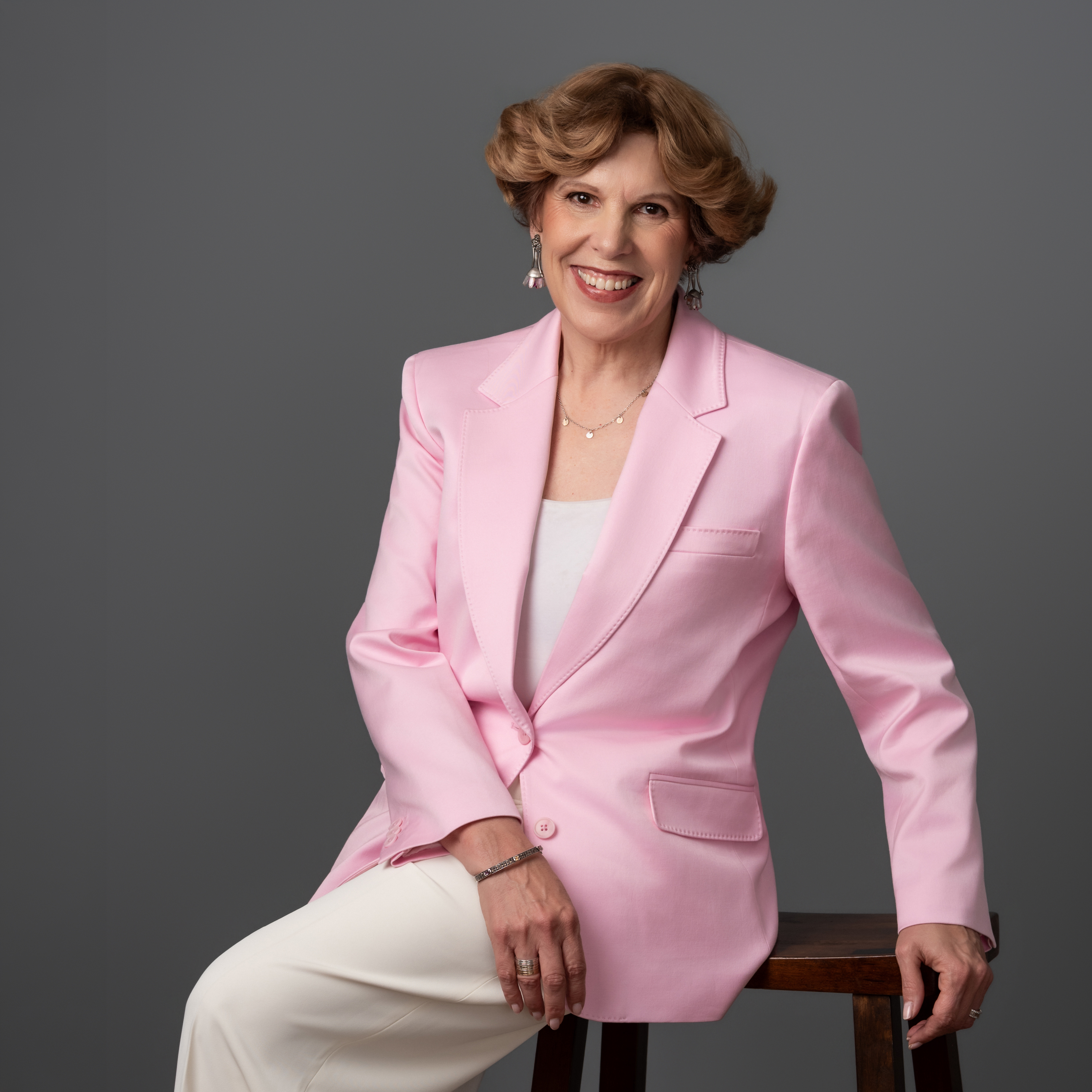 Dena Rafte seated in a pink jacket against a dark gray background