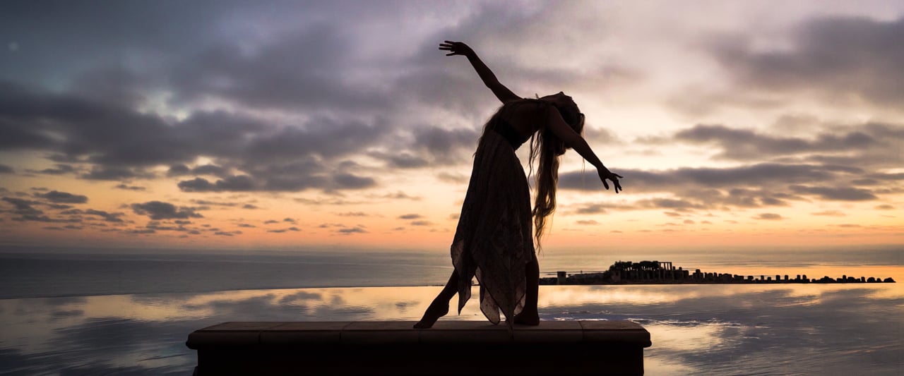 A dancer silhouetted against a glowing sky and ocean